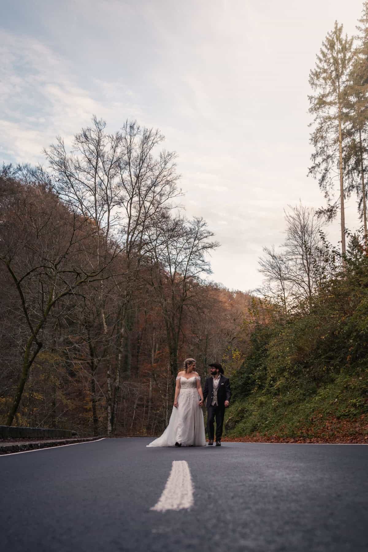 Alt: Bruid en bruidegom wandelen hand in hand op een rustige weg in de natuur in herfstkleuren.